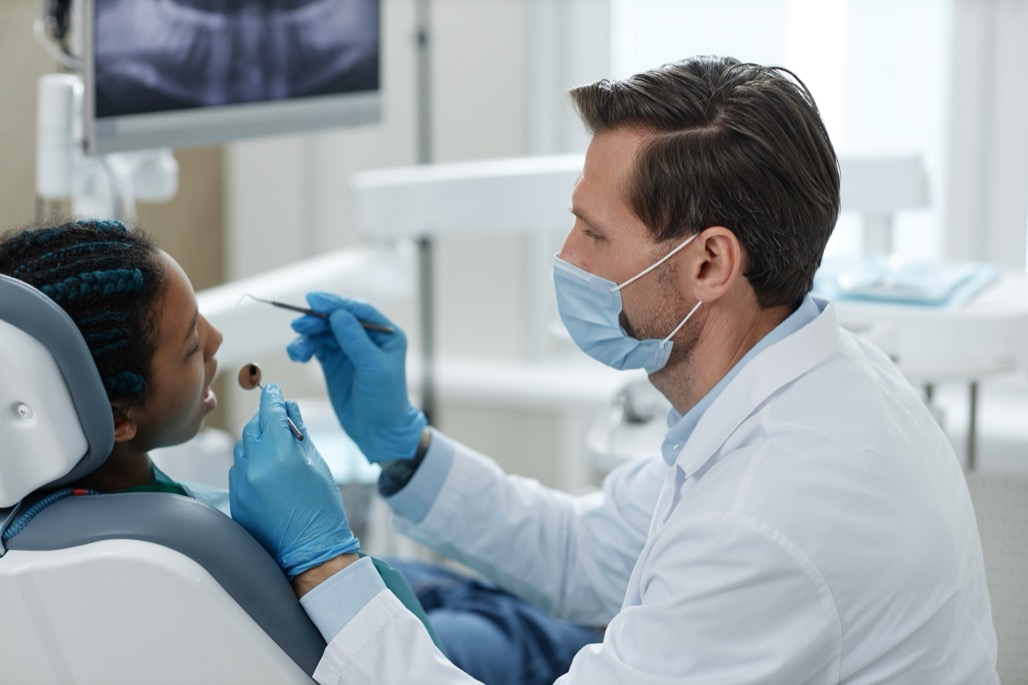 Side view portrait of male dentist wearing mask while working with child patient in clinic